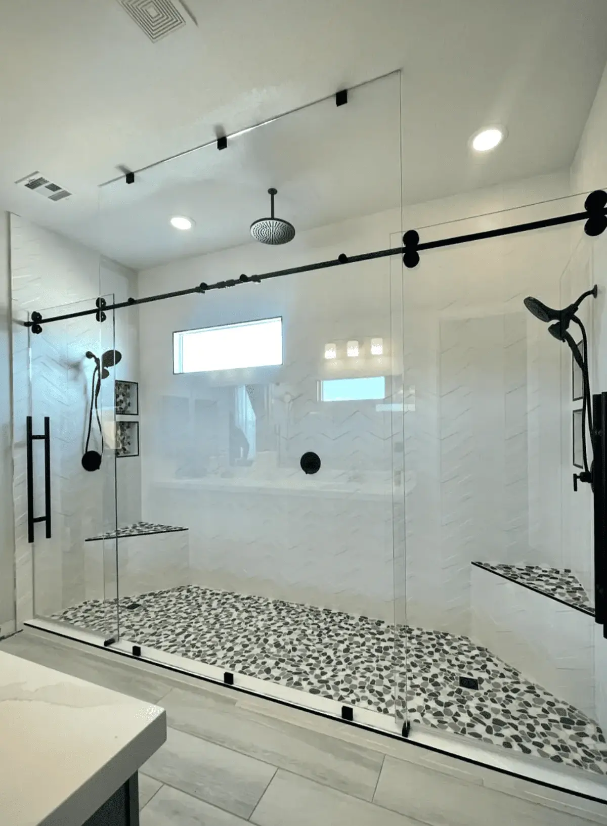 Modern frameless sliding shower doors with black hardware and pebble tile flooring by Baja Glass Las Vegas